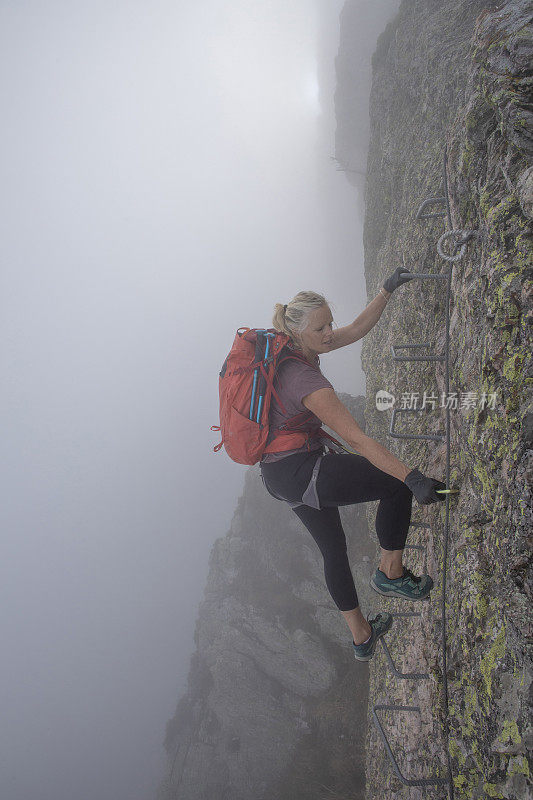 在雾中，女人爬上via ferrata的侧视图